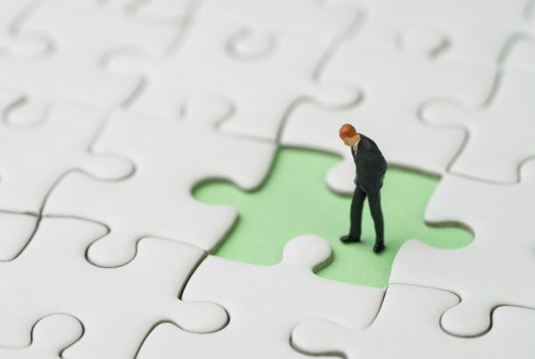 Miniature man standing on blank jigsaw puzzle piece missing