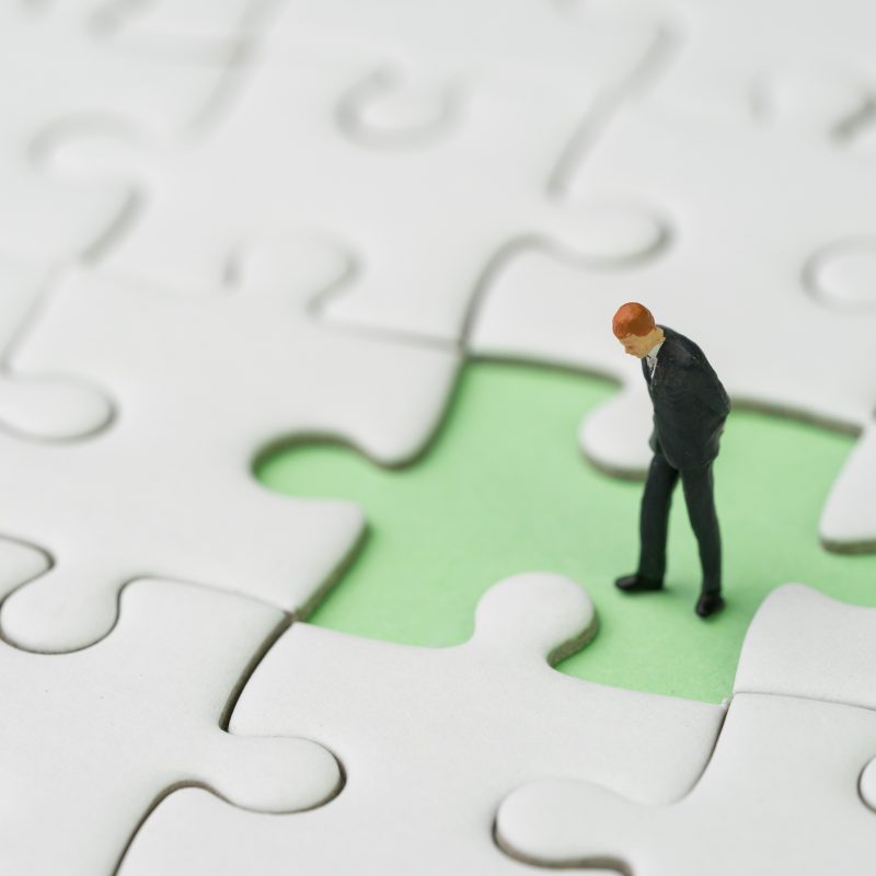 Miniature man standing on blank jigsaw puzzle piece missing