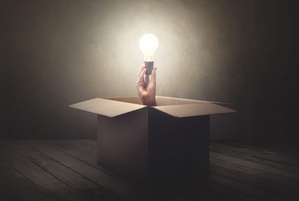 Hand coming out of cardboard box holding lightbulb Story IQ